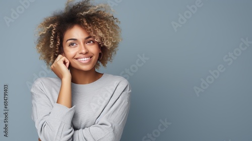 Appealing youthful african-american female student with light hair holding hand on chin and looking enchanted at upper cleared out corner as considering, posturing keen satisfied with