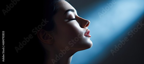  a woman with her eyes closed and her head turned to the side with a bright light shining on her face.