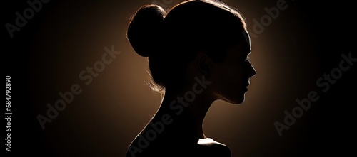  a silhouette of a woman's head with a bun in the middle of her hair, against a dark background.