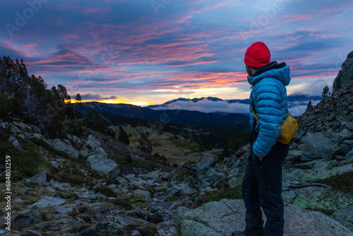 man in nature wearing winter hat, hiking in middle of mountains with lake in background looking at happy camera