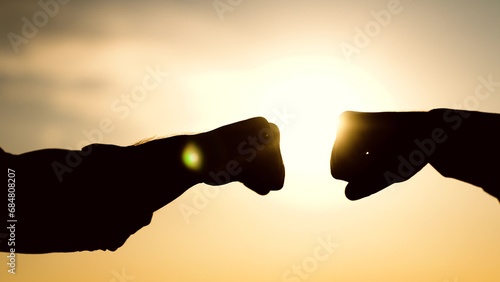 sign fists knocking sunset. business team work group people. different skin color silhouette. different nationality skin color show symbol victory success rays sunlight. hands victory close-up fist. photo