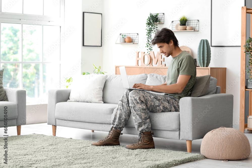 Young male soldier with laptop sitting on sofa at home Young male soldier with laptop sitting on sofa at home