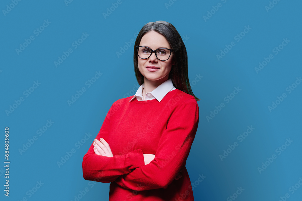 Fototapeta premium Young smiling woman with crossed arms looking at camera on blue background