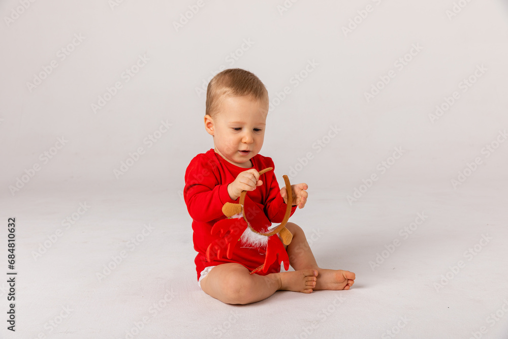 Adorable smiling child boy wearing red Christmas cap holding red christmas ball on white background. Children's emotions. Christmas and New year. The concept of an advertising banner. Adorable smiling child boy wearing red Christmas cap holding red christmas ball on white background. Children's emotions. Christmas and New year. The concept of an advertising banner.