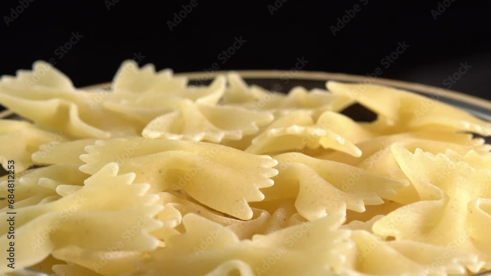 Authentic italian dry pasta farfalle closeup rotating in glass bowl. Raw dried organic golden macaroni, traditional Italy food Authentic italian dry pasta farfalle closeup rotating in glass bowl. Raw dried organic golden macaroni, traditional Italy food