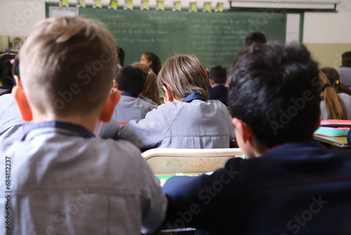 Primary school with children studying.Students in class copying text from the blackboard. Classroom with green blackboard in the background and students. Background with copy space.