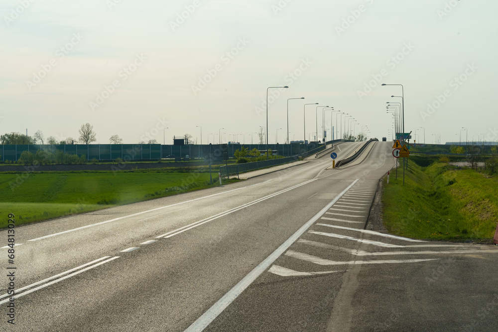 Fototapeta premium An empty road in the evening, ahead is an overpass with lanterns.