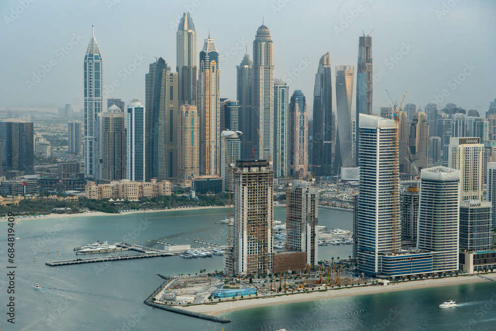 Fototapeta premium Aerial view of Dubai Marina, UAE, with many tall skyscrapers. Hazy day, boats in the marina. At sunset