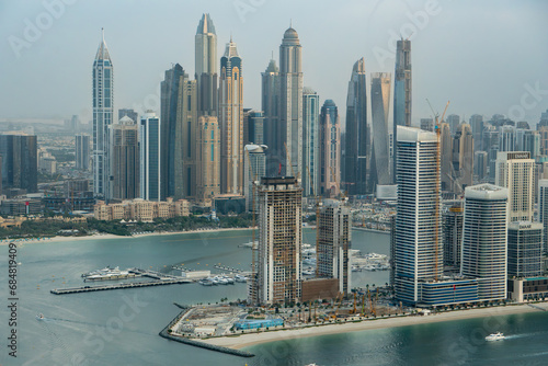 Aerial view of Dubai Marina, UAE, with many tall skyscrapers. Hazy day, boats in the marina. At sunset