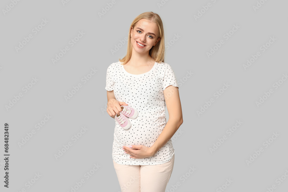 Naklejka premium Beautiful happy pregnant woman with baby shoes on grey background