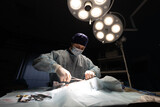 The surgeon operates under a surgical lamp. A surgeon at work in the operating room. The surgeon holds surgical instruments in his hands over the patient.