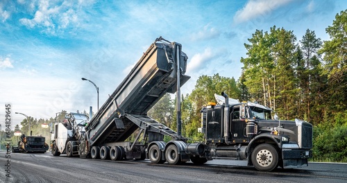 Semi-trailer truck unloading asphalt into a material transfer vehicle during paving of the Trans-Canada Highway, late in the day photo