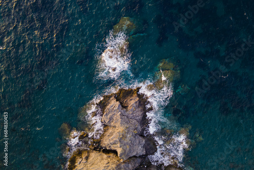 Aerial view of Sea waves crashing and white foaming on empty big rock stones seashore. Wild sea washing reef rock cliff