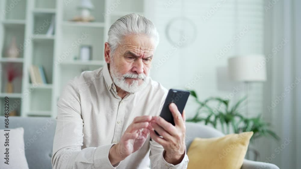 Frustrated elderly senior man having problems with software or service on smartphone sitting on sofa in living room at home. Worried disappointed mature male complains about bad internet connection Frustrated elderly senior man having problems with software or service on smartphone sitting on sofa in living room at home. Worried disappointed mature male complains about bad internet connection