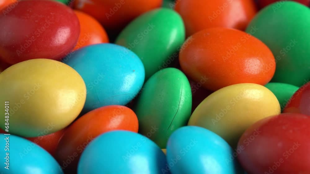 Sweet dragees in colored glaze are rotating background macro side light. Delicious sweets and candies close-up that children like. Chocolate Coating