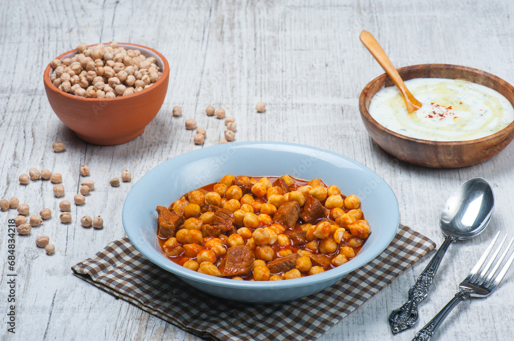 High angle view image of traditional Turkish chickpea dish with meat with a tzatiki bowl in the background High angle view image of traditional Turkish chickpea dish with meat with a tzatiki bowl in the background
