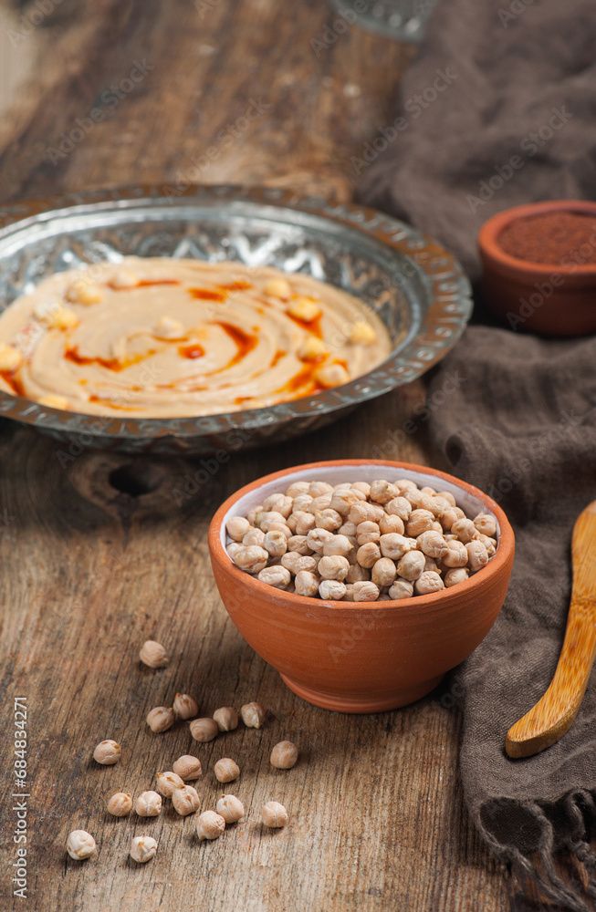 High angle photo of a bowl of raw chickpeas with a humus plate in the background High angle photo of a bowl of raw chickpeas with a humus plate in the background