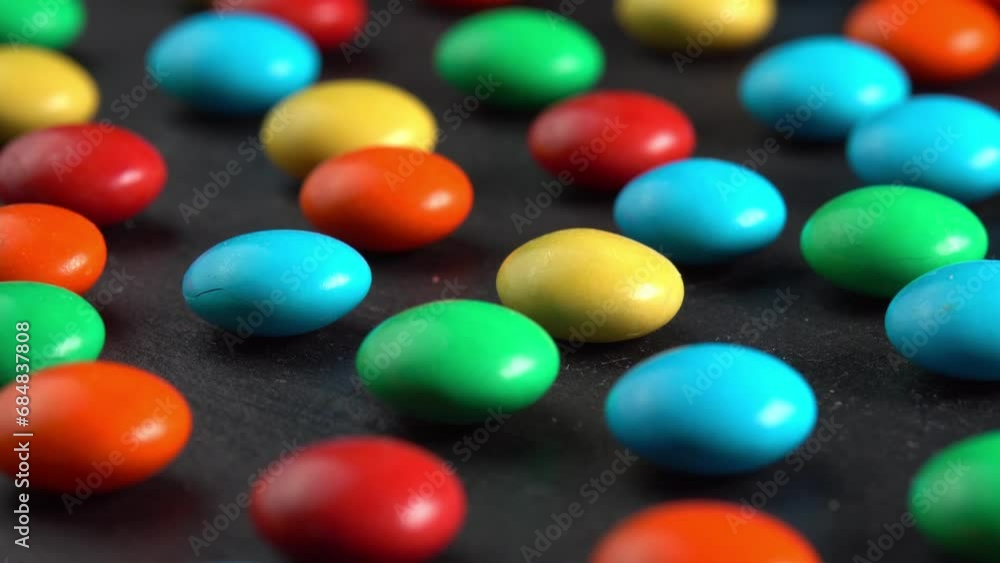 Sweet dragees in colored glaze rotating on black plate background macro side view sun light. Delicious sweets and candies close-up that children like. Chocolate Coating Sweet dragees in colored glaze rotating on black plate background macro side view sun light. Delicious sweets and candies close-up that children like. Chocolate Coating