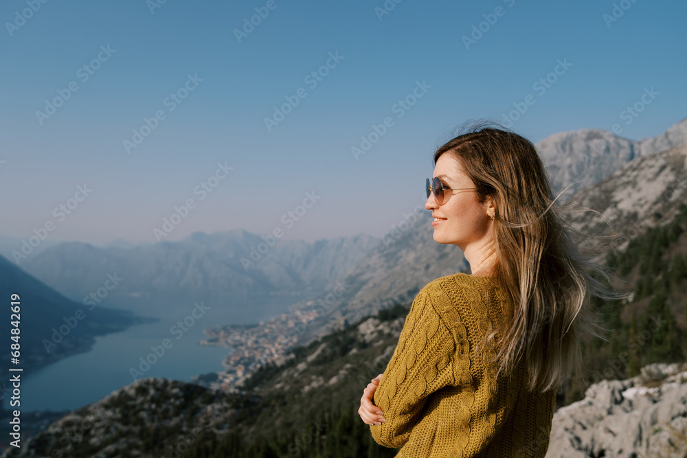 Smiling girl in sunglasses stands on a mountain above the Bay of Kotor. Montenegro. Side view