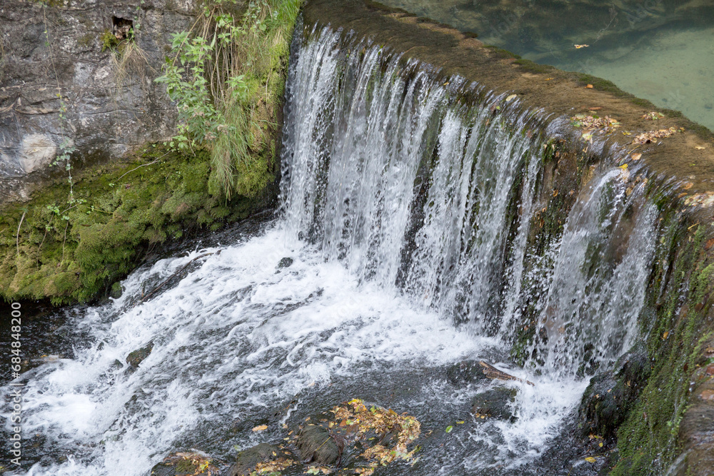 Fototapeta premium A small waterfall created by a concrete dam at the source of Krupajsko vrelo. Close up, movement, water flowing.