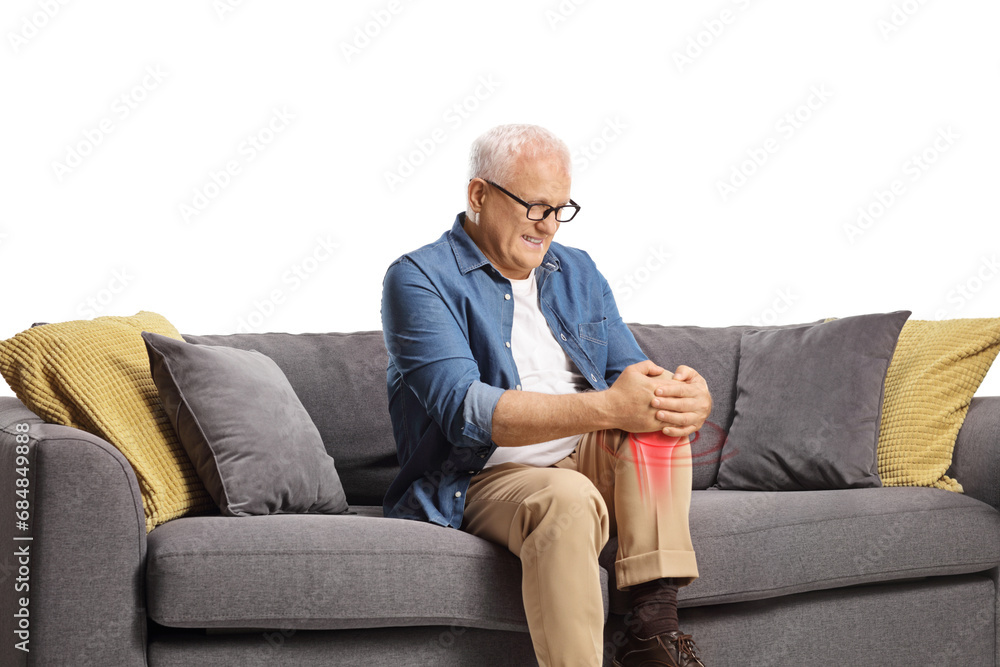 Mature man in pain sitting on a sofa and holding his red inflamed knee