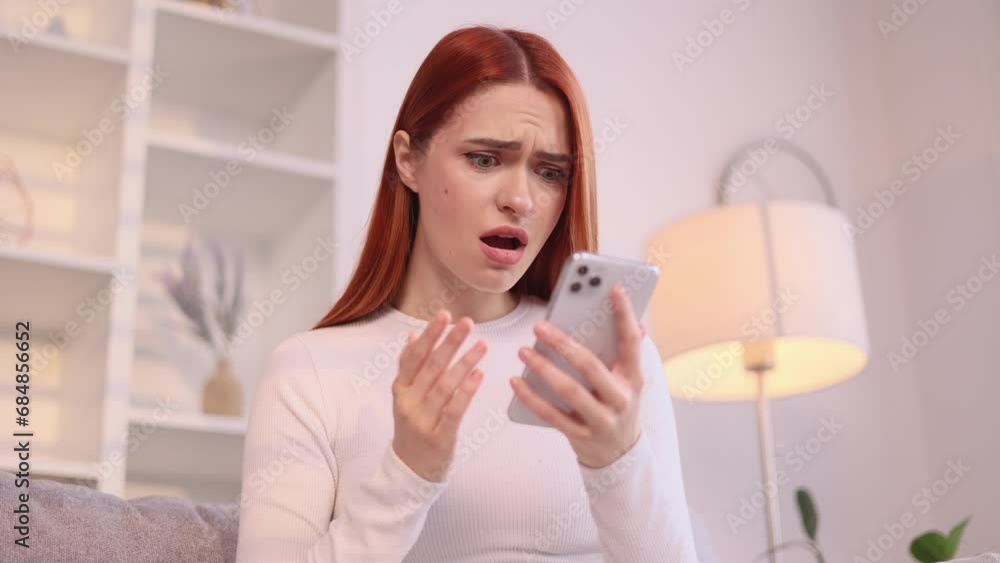 Attractive young red haired woman at home get notification and feeling upset reading bad negative news message on smartphone and looking at screen indoors Disappointment Fail Unemployment Attractive young red haired woman at home get notification and feeling upset reading bad negative news message on smartphone and looking at screen indoors Disappointment Fail Unemployment