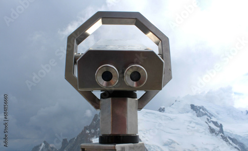 Coin-operated binoculars pointing to a snowy mountain and clouds