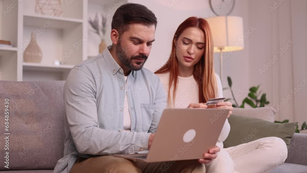 Cute young family couple paying with credit card on laptop computer together sitting on couch at home Happy customers doing payments online in internet store indoors Cute young family couple paying with credit card on laptop computer together sitting on couch at home Happy customers doing payments online in internet store indoors