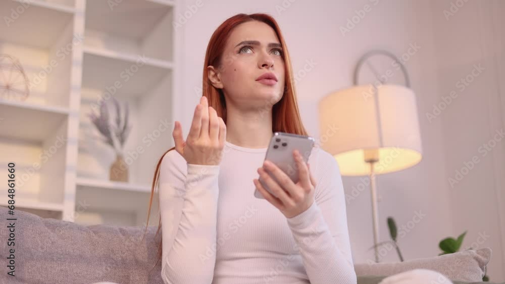Portrait of creative red haired woman student hold smartphone and thinks questioningly about difficult choice choose imagine plan in mind has doubts create idea sitting on couch at home Portrait of creative red haired woman student hold smartphone and thinks questioningly about difficult choice choose imagine plan in mind has doubts create idea sitting on couch at home