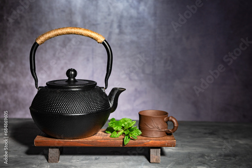 Traditional Asian cast-iron kettle with clay cup on a wooden stand. photo