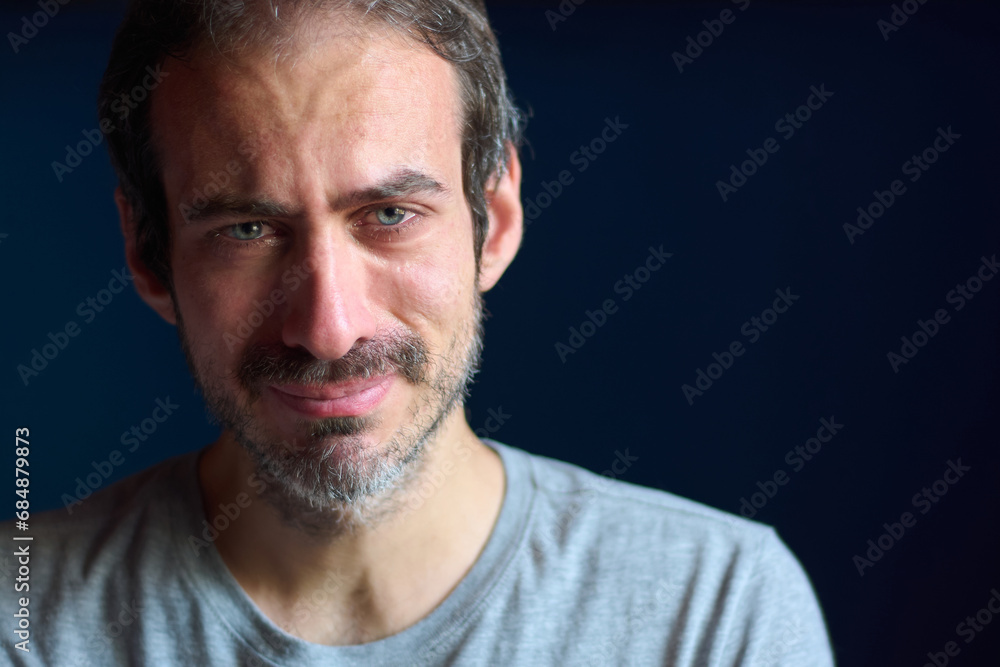Close up of young caucasian 30 year old man with short beard and blue eyes crying while looking at the camera. Concept of depression, loss and grief. Emotional trauma. Close up of young caucasian 30 year old man with short beard and blue eyes crying while looking at the camera. Concept of depression, loss and grief. Emotional trauma.