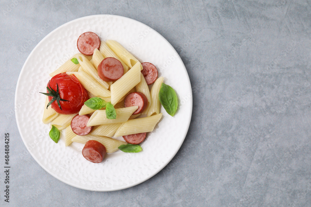 Tasty pasta with smoked sausage, tomato and basil on light grey table, top view. Space for text