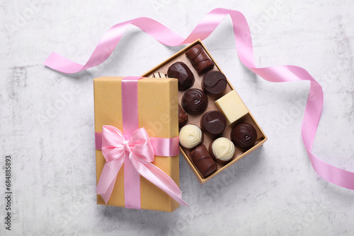 Open box with delicious chocolate candies and pink ribbon on white table, top view