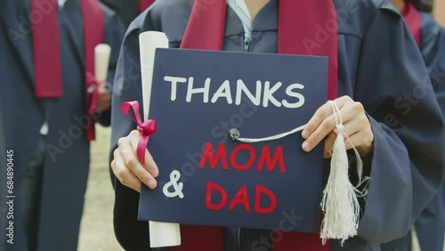 Cropped shot of unrecognizable female student holding university hat with text thanks mom and dad during graduation ceremony photo