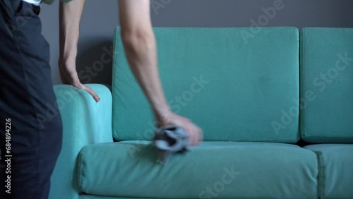 worker with yellow microfiber rag cleaning sofa textile at home