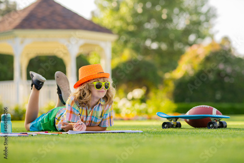 Summer leisure with children. School boy in park outdoor doing school homework. Child kid writing in notebook with pencil outside. Outdoor learning studying.