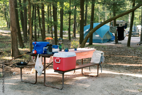 Slika na platnu Horizontal image of a campsite picnic table with a water jug and cooler sitting on top