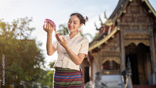 A charming Thai woman in a traditional Thai-Lanna dress is admiring a beautiful garland in her hand.