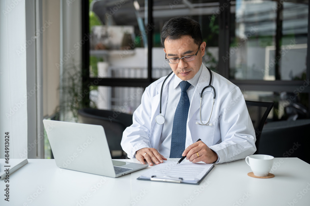An experienced Asian senior male doctor is examining medical cases on report at his desk. An experienced Asian senior male doctor is examining medical cases on report at his desk.