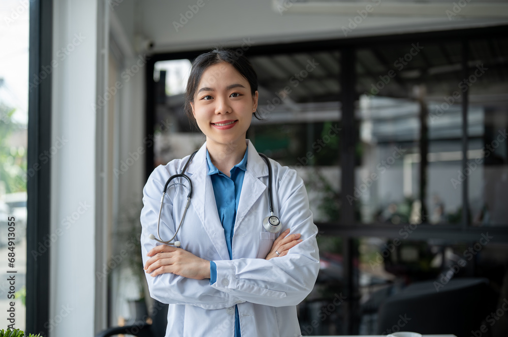 A beautiful Asian female doctor in a white gown is standing in the office with her arms crossed. A beautiful Asian female doctor in a white gown is standing in the office with her arms crossed.