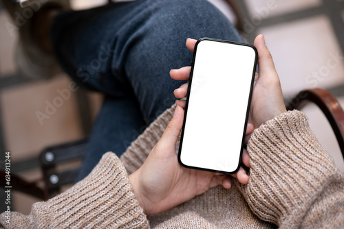 Close-up image of a woman in casual clothes is using her smartphone while sitting outdoors.