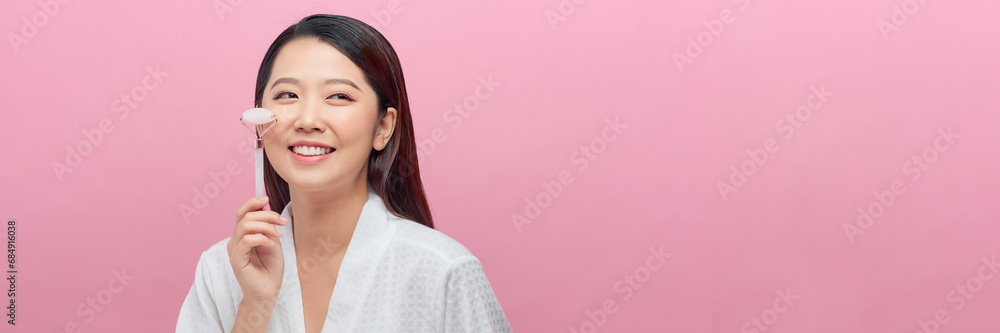 Portrait Asian woman doing face massage with jade smiling isolated on pink banner background Portrait Asian woman doing face massage with jade smiling isolated on pink banner background