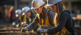 Women wearing hardhats lugging about hollow, flat clay bricks in a group while storing building supplies outside. .