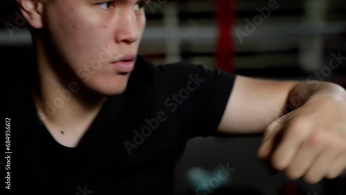 A determined man stands indoors, his wrist cocked and neck tense, ready to unleash his powerful fist upon the world with a flex of his elbow and the strength of his shoulder and muscles, his finger