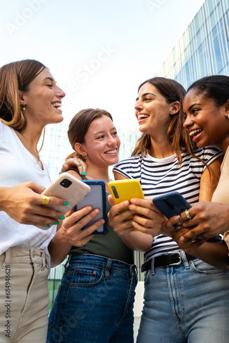 Vertical portrait of happy multiracial group of young women friends laughing and having fun while using mobile phones.