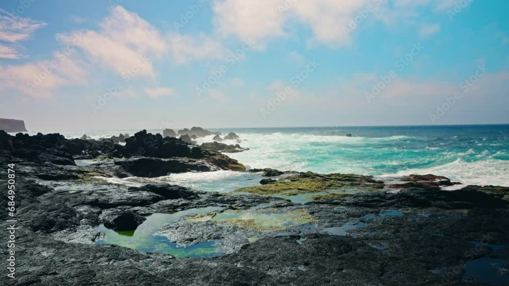 Slow motion shot of rough ocean waves crushing against the volcanic rocky coastline. Colorful turquoise sea water splashing against the shore. Sunny day, clear blue sky. Slow motion shot of rough ocean waves crushing against the volcanic rocky coastline. Colorful turquoise sea water splashing against the shore. Sunny day, clear blue sky.