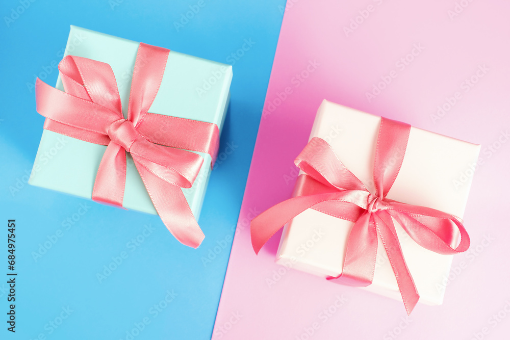 Three gift boxes with ribbons on pink and blue background close-up, top view. Three gift boxes with ribbons on pink and blue background close-up, top view.