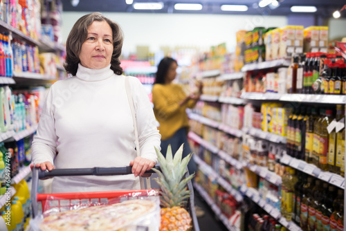 Casual aged woman doing shopping in grocery department of supermarket