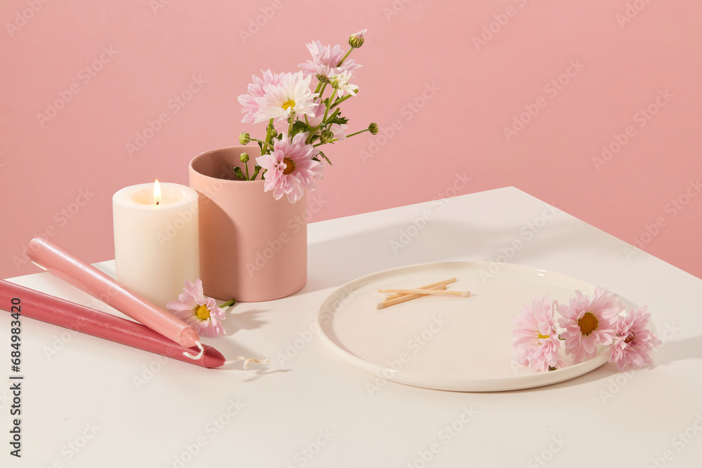 On the white table there are candles, fresh flowers, a ceramic cup and a ceramic plate with a pink background. Space for product display. Beauty theme. On the white table there are candles, fresh flowers, a ceramic cup and a ceramic plate with a pink background. Space for product display. Beauty theme.