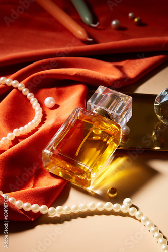 A bottle of perfume without label is displayed on a table with a string of pearls  candles and red silk. Mockup for perfume advertisement with blank label.